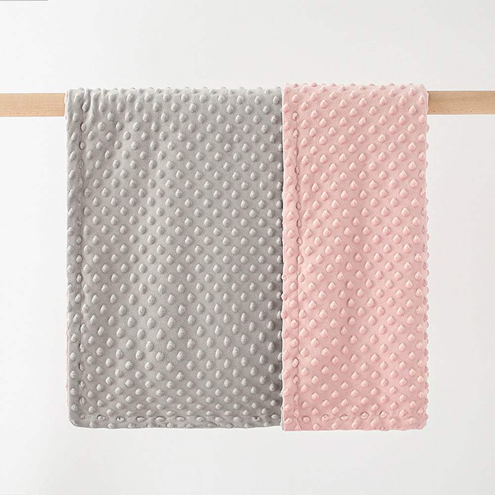Soft double-layer baby blanket with dotted texture in gray and pink colors hanging on wooden rod