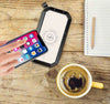 wireless solar powerbank charging smartphone on wooden table next to coffee cup and notebook
