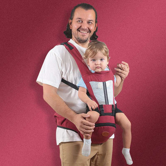 Man carrying toddler in red baby hip seat carrier with adjustable straps and pocket against red background