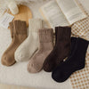 Thickened wool tube soft socks in brown, beige, and black colors with ribbed cuffs on cozy surface next to book and candle