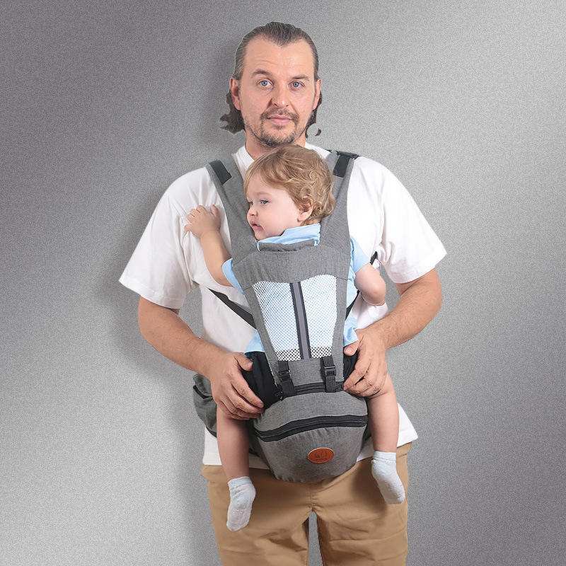Man wearing grey ergonomic baby hip seat carrier with toddler facing forward