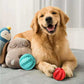 Golden retriever dog playing with red and blue chew-resistant treat balls toy on a gray surface with plush toys in the background