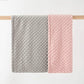 Soft double-layer baby blanket with dotted texture in gray and pink colors hanging on wooden rod