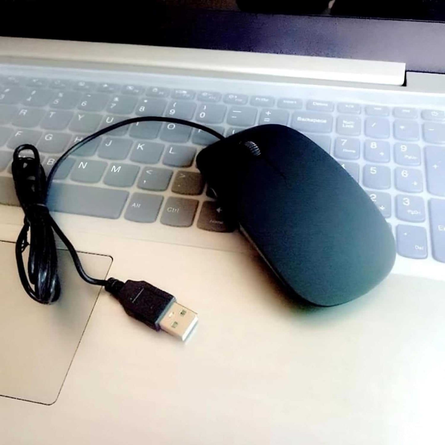 Black ultra-slim optical wired mouse with scroll wheel and USB 2.0 connector on laptop keyboard