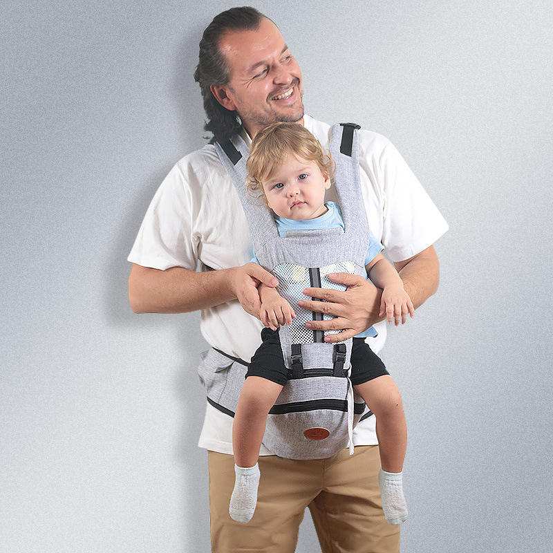 Baby hip seat carrier worn by man carrying toddler with adjustable straps and ergonomic design