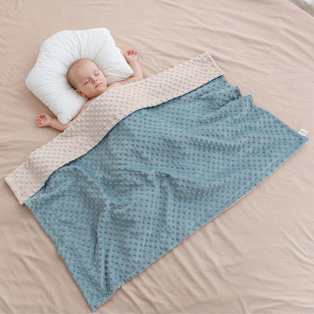 Newborn baby sleeping under a super soft double-layer baby blanket with dotted backing on beige bedding