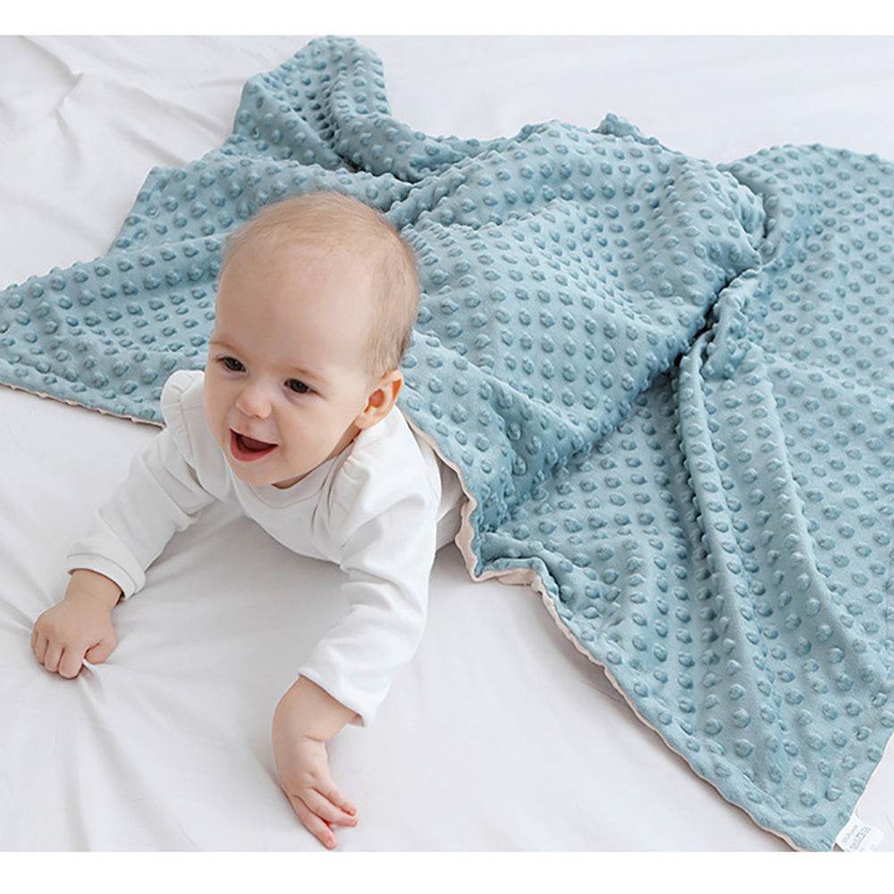 Baby wrapped in super soft double-layer blue baby blanket with dotted texture on white bed